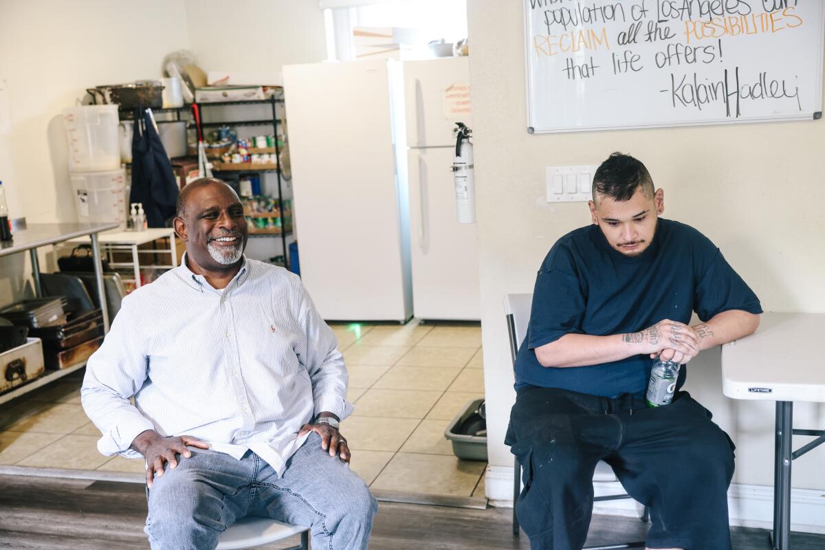 Kalain Hadley, left, smiles as he and another resident sit near a small kitchen in a halfway house.