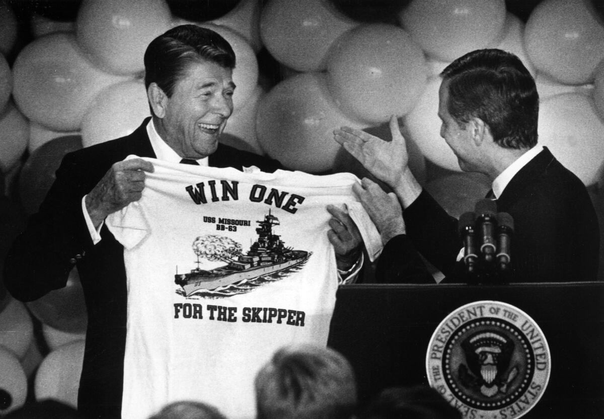 A person holds up a T-shirt with the words "Win One for the Skipper" to show it to another person.