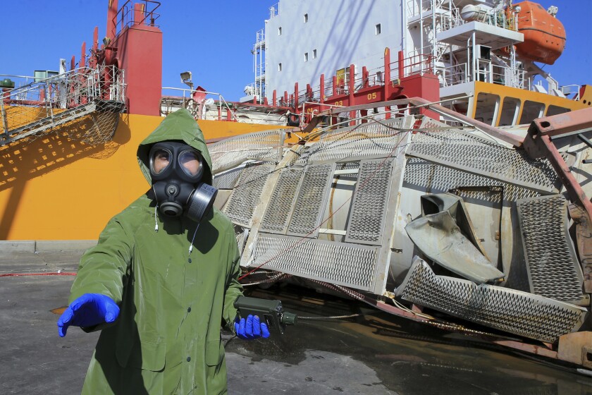 CORRECTS DAY TO TUESDAY -- Experts investigate at the site of a toxic gas explosion in Jordan's Red Sea port of Aqaba, Tuesday, June 28, 2022. A crane loading chlorine tanks onto a ship on Monday dropped one of them, causing an explosion of toxic yellow smoke that killed over a dozen people and sickened some 250, authorities said. (AP Photo/Raad Adayleh)