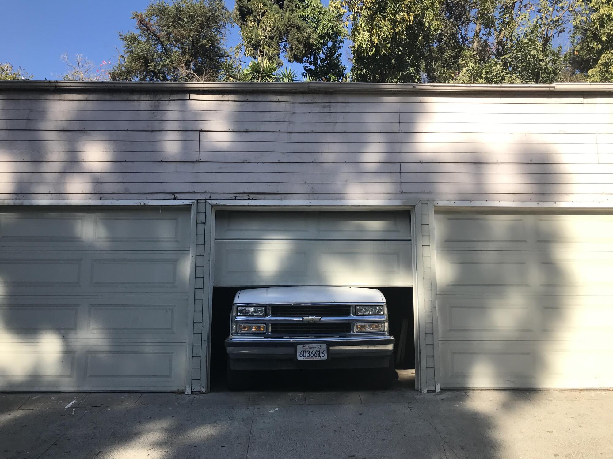 The front end of a large pick-up truck pokes out of a partially closed garage door. 