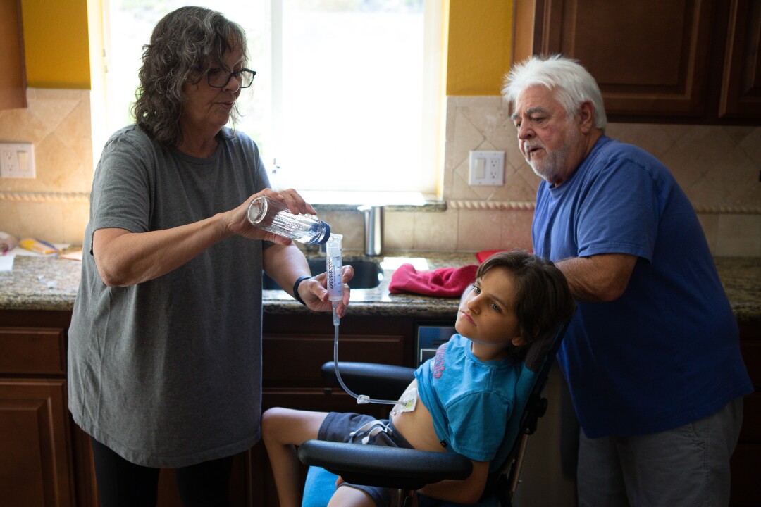 Mary and Bob Cunningham give their grandson Connor Dalby water through his feeding tube at their home.