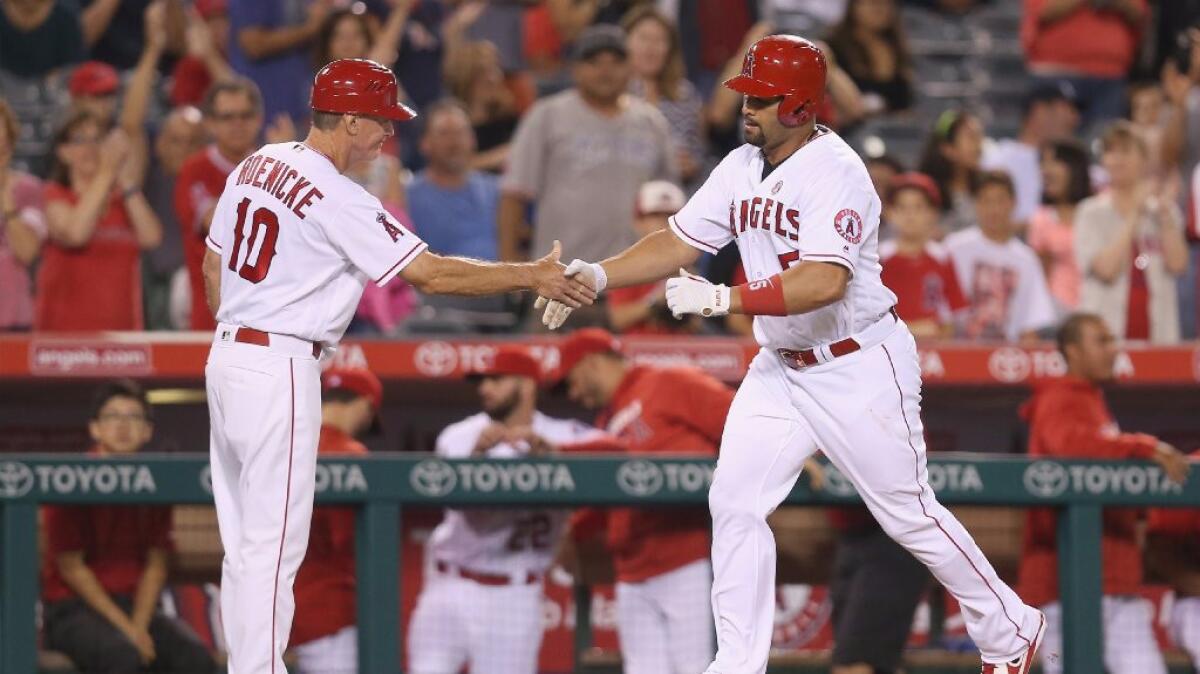 Angels first baseman Albert Pujols is greeted by third base coach Ron Roenicke after hitting a solo home run in the ninth inning of a game on Saturday.