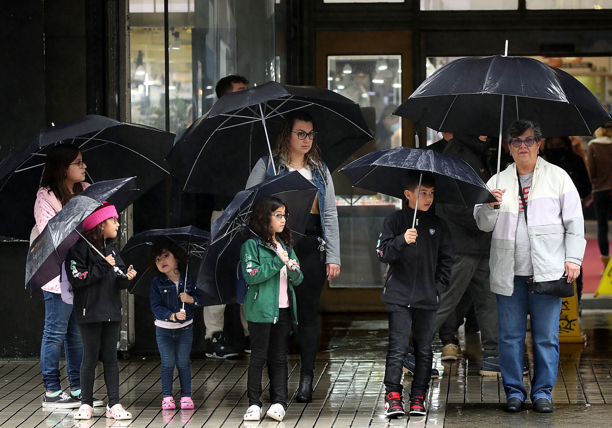 The Arzate family, visiting from Phoenix, wait to cross Hill Street in downtown Los Angeles on a rainy Wednesday