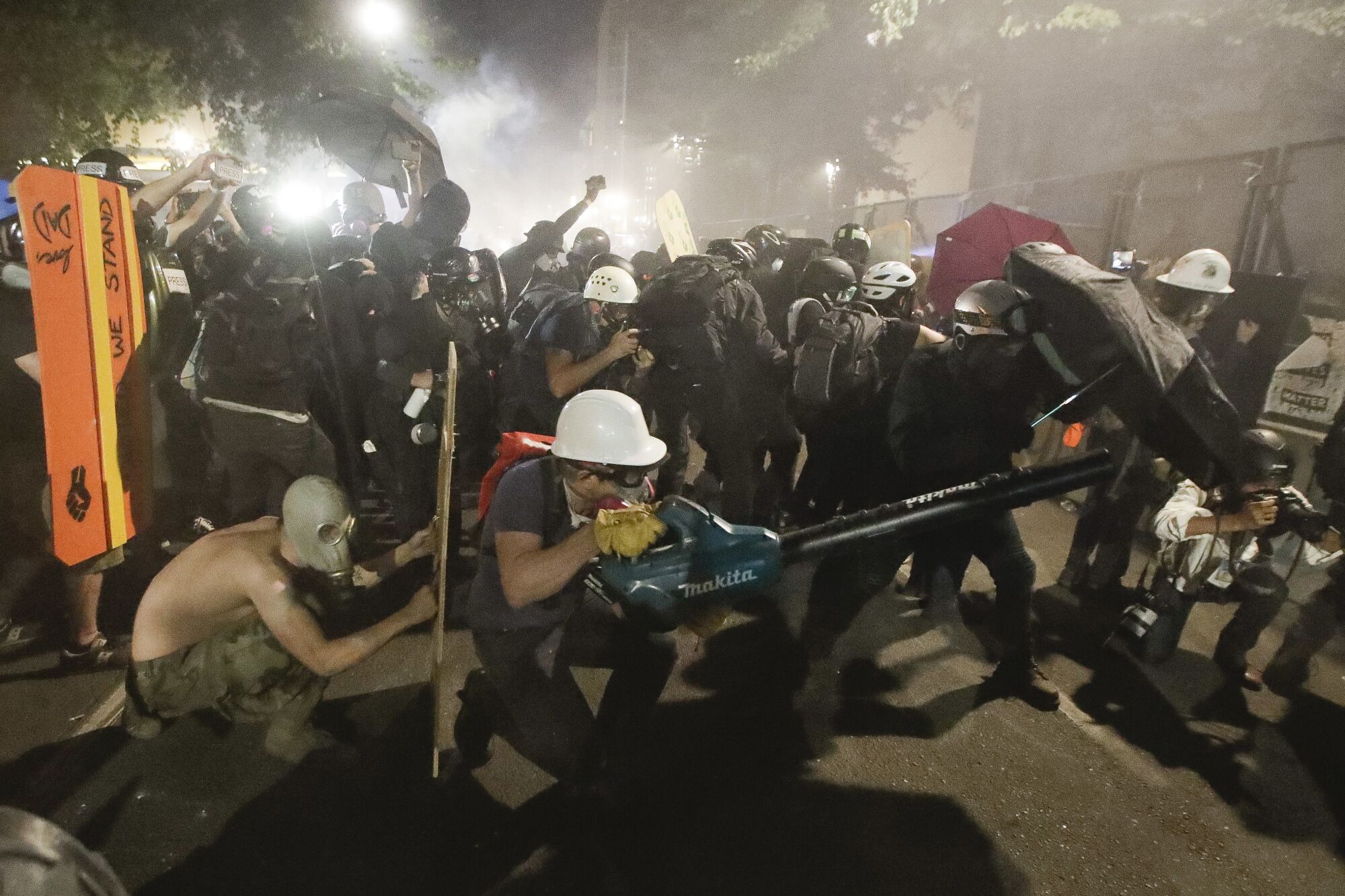 Demonstrators huddle and blow back tear gas with leaf blowers during a clash with federal officers.