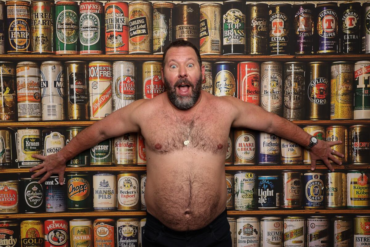 Bert Kreischer poses shirtless in front of beer cans.