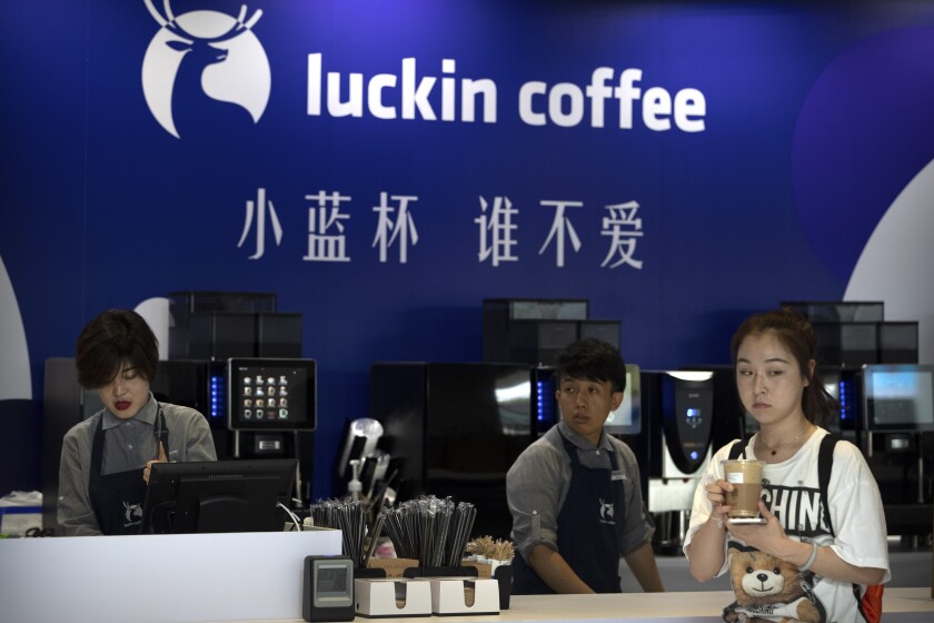 FILE - In this Aug. 15, 2018, photo, a customer picks up her order from a Luckin Coffee pop-up shop at the World Robot Conference in Beijing. China’s Luckin Coffee has filed for bankruptcy protection. The Chinese rival to Starbucks said Friday, Feb. 5, 2021 that it is negotiating with stakeholders regarding the restructuring of its financial obligations, to strengthen its balance sheet and to allow it to emerge as a going concern. (AP Photo/Mark Schiefelbein, File)