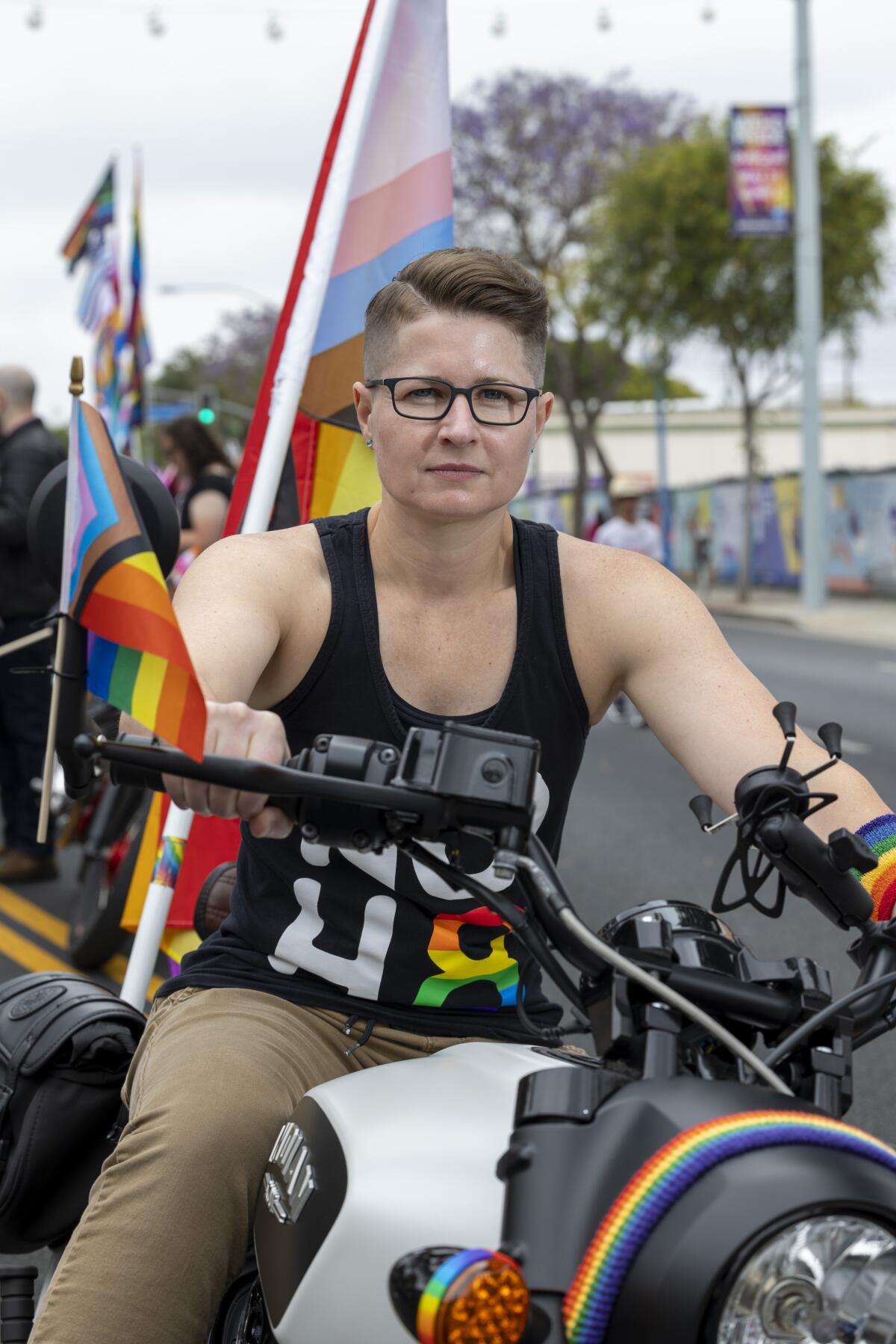 A person in a black tank top and glasses rides a motorcycle.