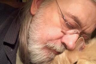Caleb Carr, with glasses and a white beard, nestles his face on his cat Masha's head. 
