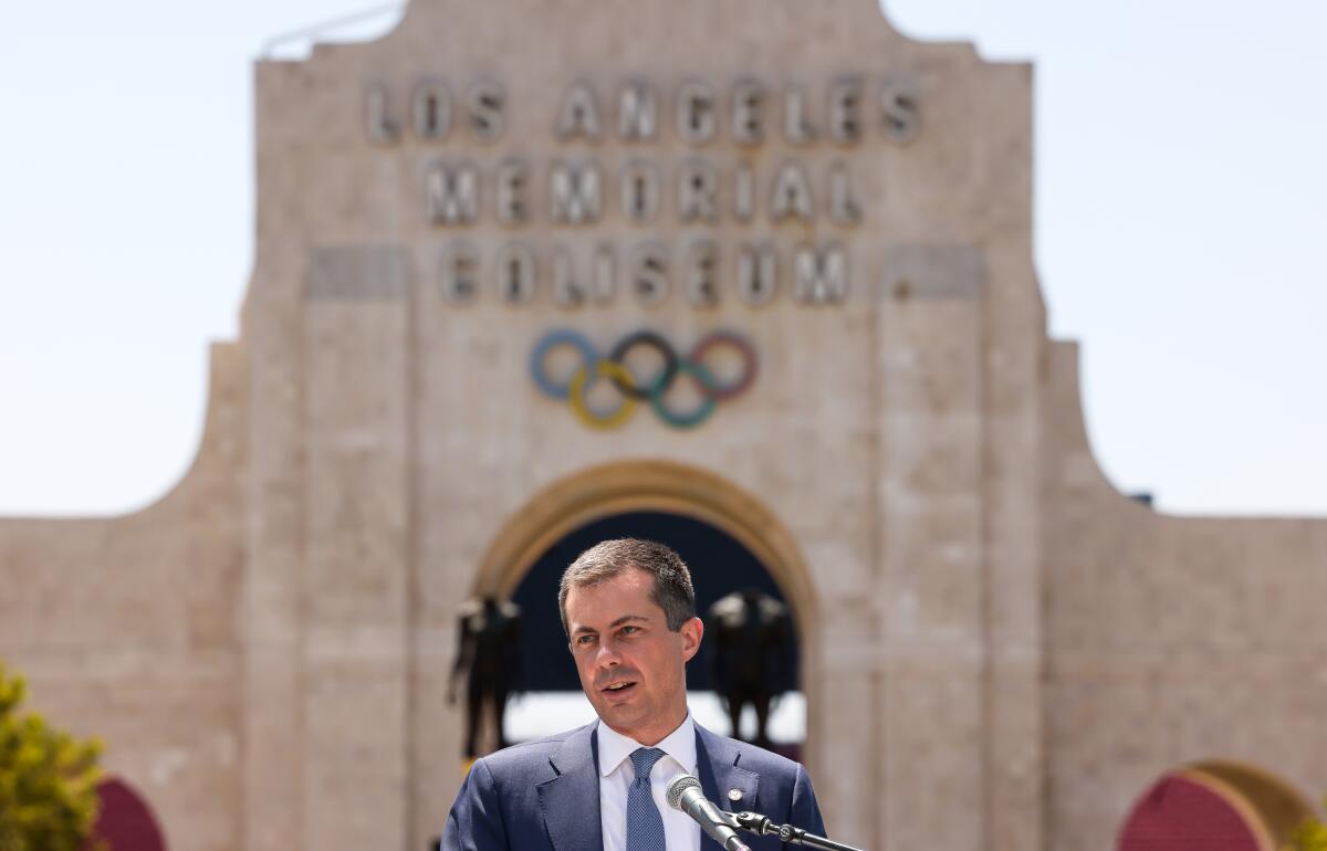 Transportation Secretary Pete Buttigieg speaks into a microphone with the Los Angeles Memorial Coliseum behind him
