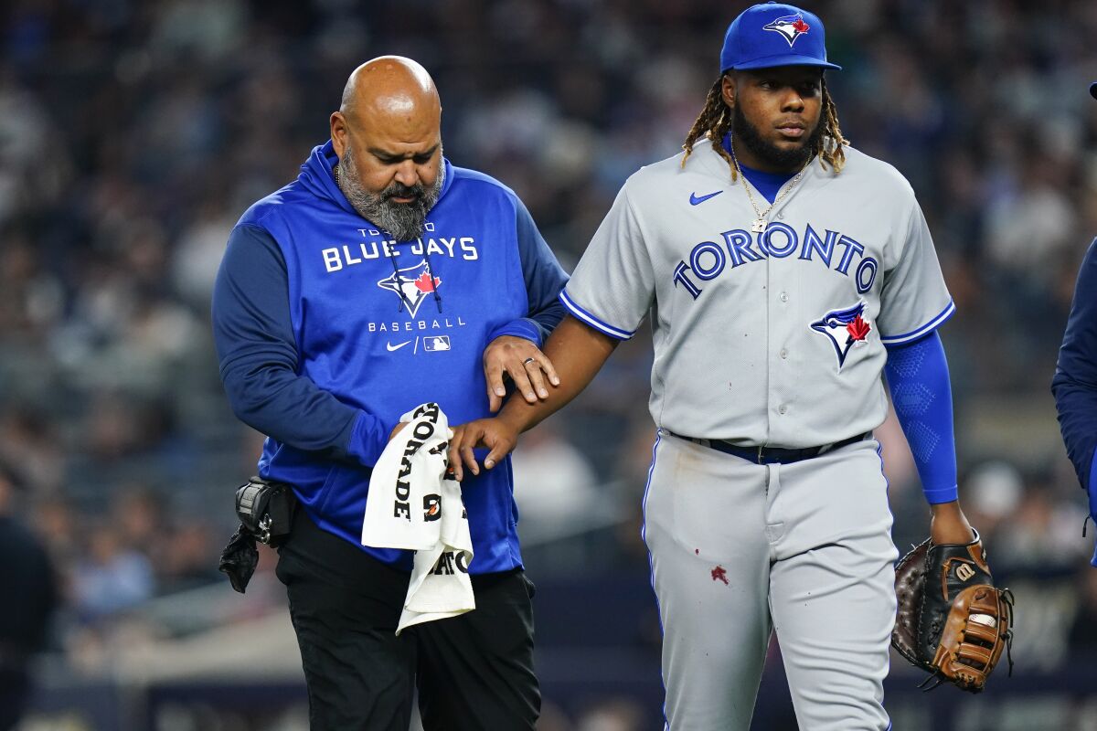 A trainer helps Toronto Blue Jays first baseman Vladimir Guerrero Jr., who injured his hand during the second inning of the team's baseball game against the New York Yankees on Wednesday, April 13, 2022, in New York. (AP Photo/Frank Franklin II)