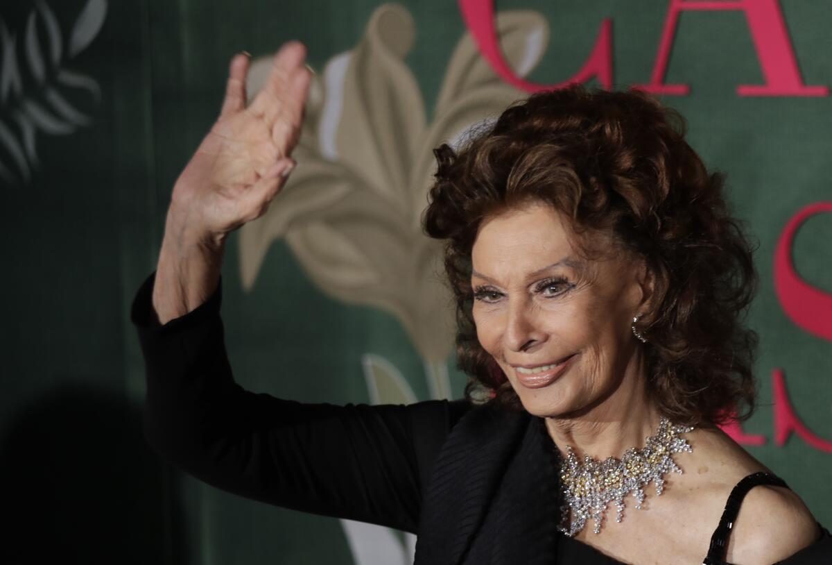 Sophia Loren waves and smiles in a black gown and diamond necklace