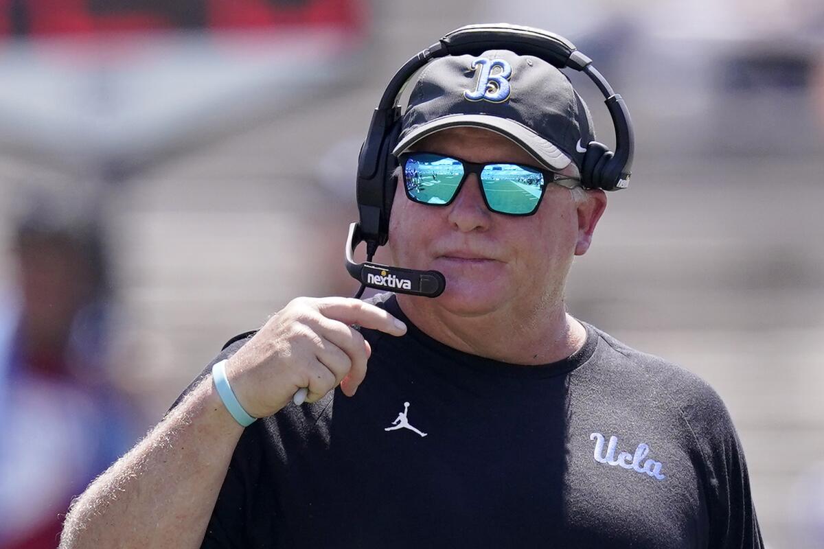 UCLA coach Chip Kelly wears mirrored sunglasses while talking into a headset on the sideline.