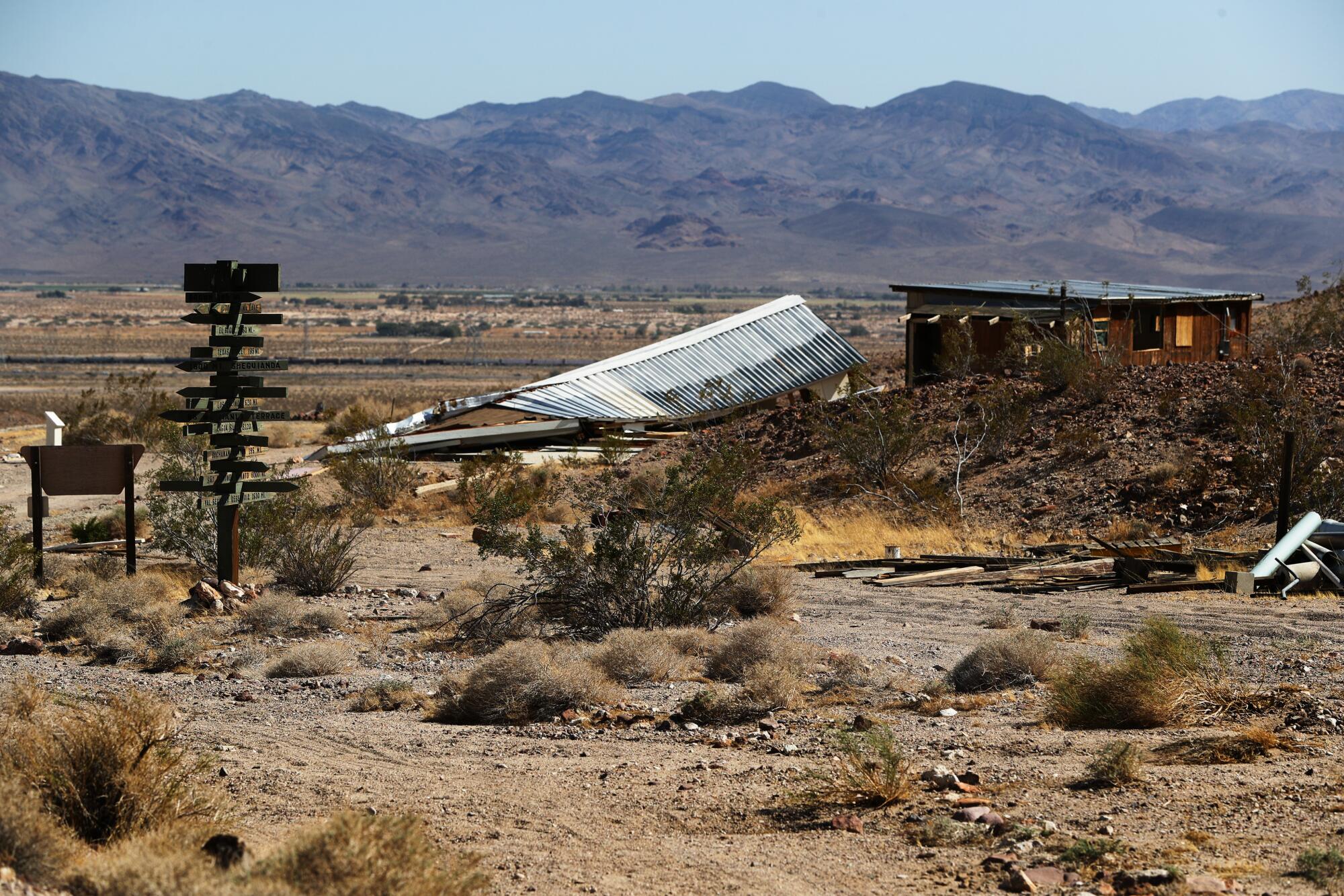 A collapsed corrugated steel roof lies in the desert.