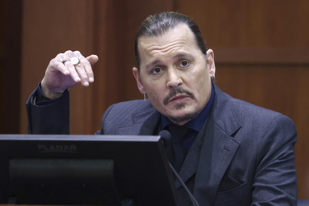 A man in a dark suit and tie gestures with his right hand while testifying in court
