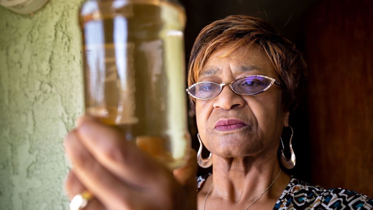 Sativa customer Karen Lewis holds a jar of brown water that came from her faucet.