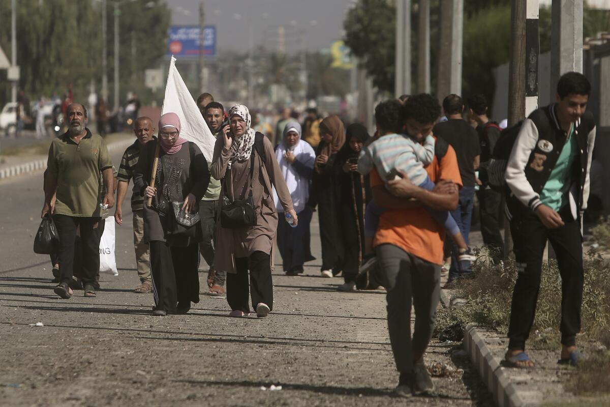 A woman carries a white flag to prevent being shot as she walks among other civilians.