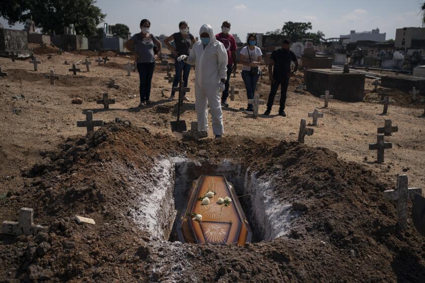 A cemetery worker stands before the coffin containing the remains of Edenir Rezende Bessa, who is suspected to have died of COVID-19, as relatives attend her burial, in Rio de Janeiro, Brazil, Wednesday, April 22, 2020. After visiting 3 primary care health units she was accepted in a hospital that treats new coronavirus cases, where she died on Tuesday. “People need to believe that this is serious, it kills", said her son Rodrigo Bessa who works at a hospital as nurse in the Espirito Santo state. (AP Photo/Leo Correa)
