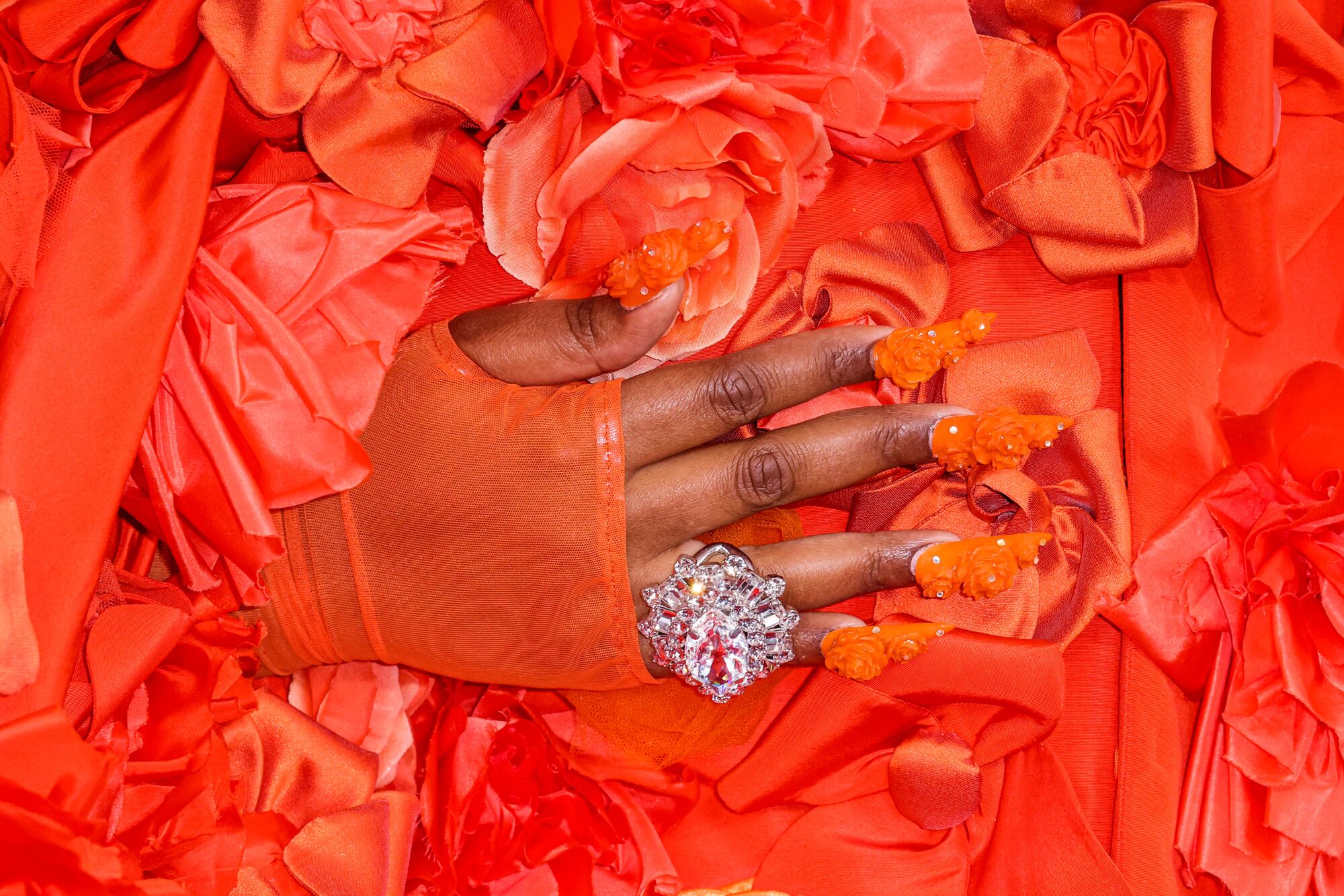 A hand with a big ornate ring holds a red outfit made of flowers.