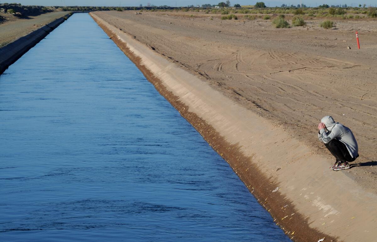 Un solicitante de asilo espera pensativo al borde de un canal de riego en la frontera entre México y Estados Unidos