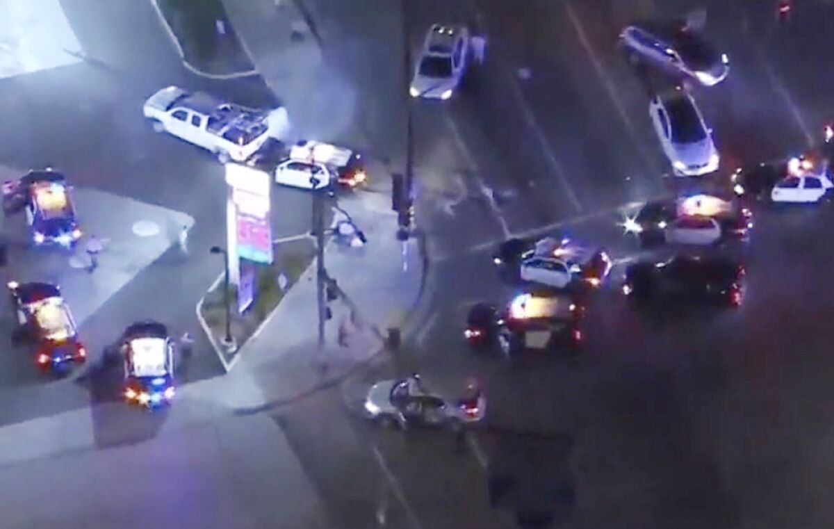 An aerial view of police cars surrounding a white pick up truck and other vehicles at a gas station. 