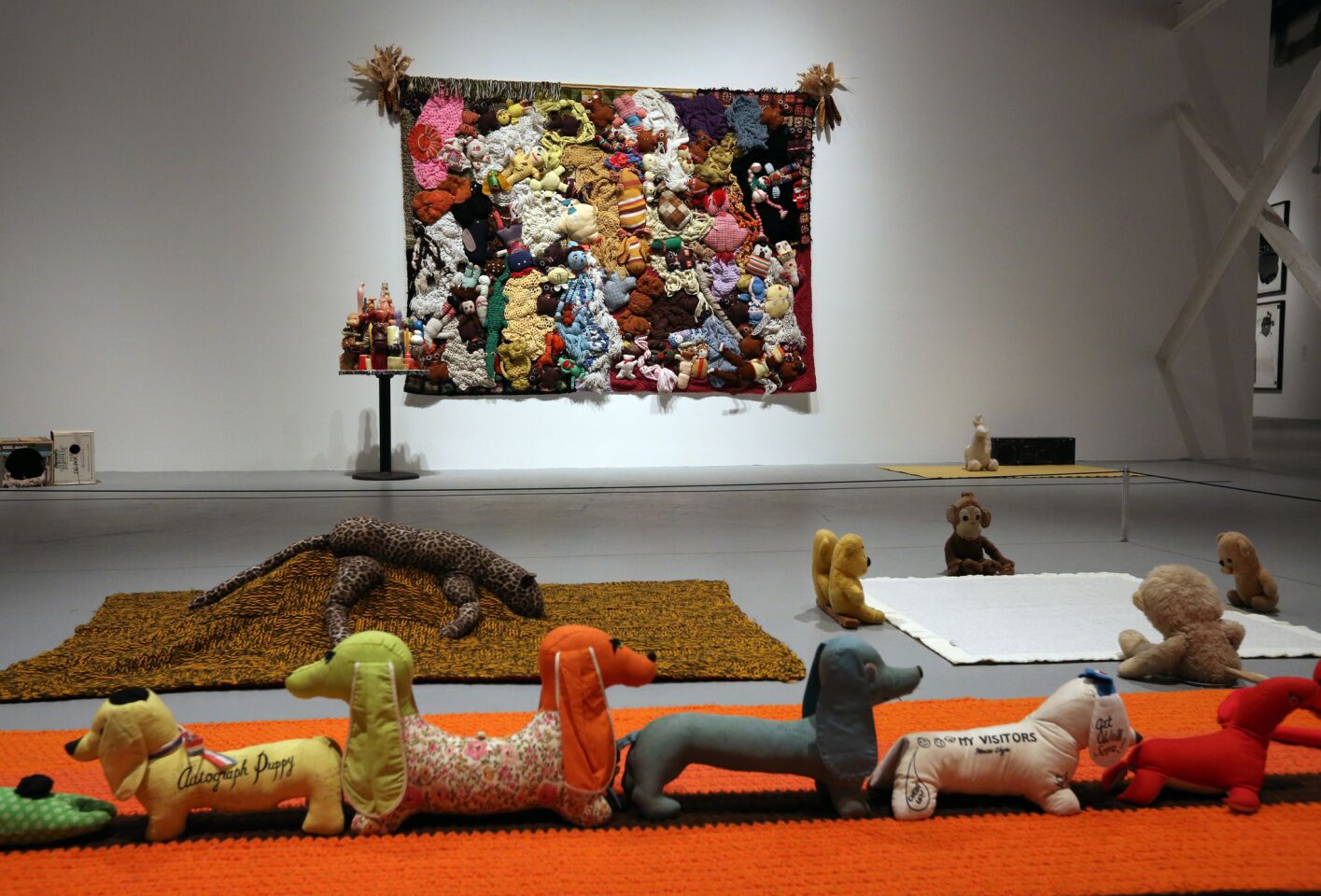 Stuffed animals from Mike Kelley's "Arena" series march along the floor of MOCA's Geffen Contemporary in the foreground. In the background is the late L.A. artist's "More Love Hours Than Can Ever Be Repaid," a large crocheted wall-hanging with stuffed animals. Both are part of a Kelley retrospective at the Geffen.