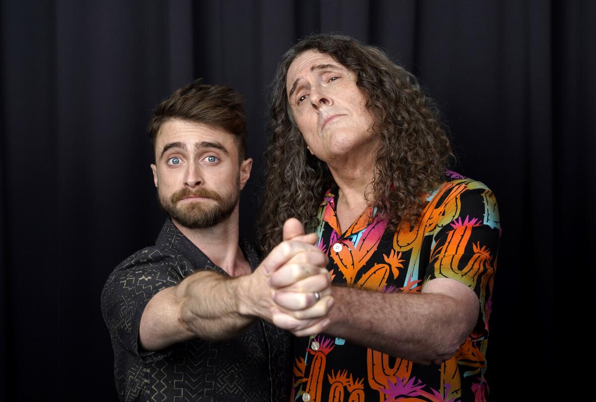 Daniel Radcliffe and Weird Al Yankovic pose in a tango-like embrace for a portrait.