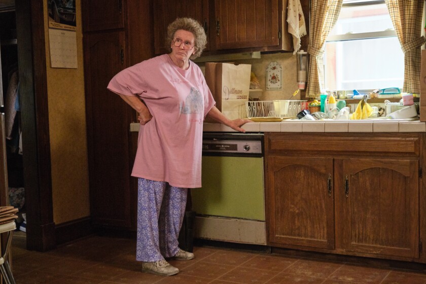Mamaw, played by Glenn Close, stands in the middle of the kitchen in  patterned purple pajamas and a pink T-shirt