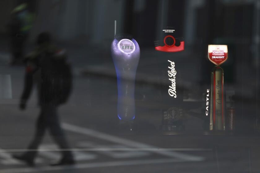 FILE - In this May 7, 2020, file photo, beer taps of South African Brewery brands are seen through the window of a closed bar in Cape Town, South Africa. A bootlegging culture has sprung up across South Africa in response to the government's nearly 8-week-old ban on the sale of cigarettes and alcohol. (AP Photo/Nardus Engelbrecht, File)