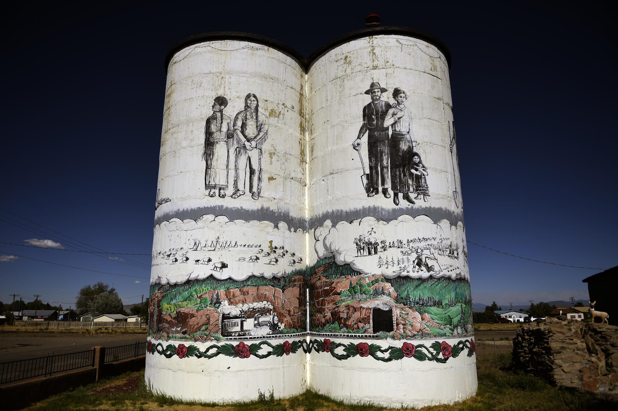 Murals on two large white columns depict two people on each, with green and brown mountains on the lower portions