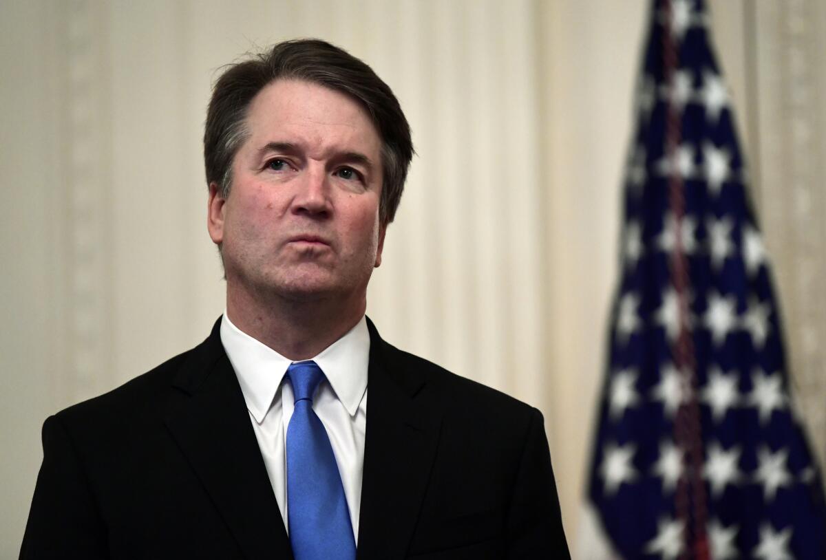 Supreme Court Justice Brett M. Kavanaugh stands near a U.S. flag