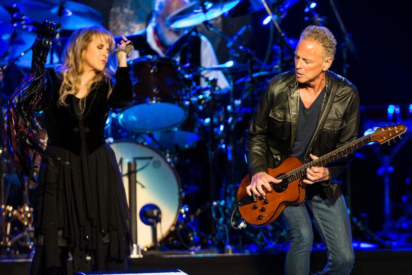 A woman in a black dress and a man with a guitar perform with a band