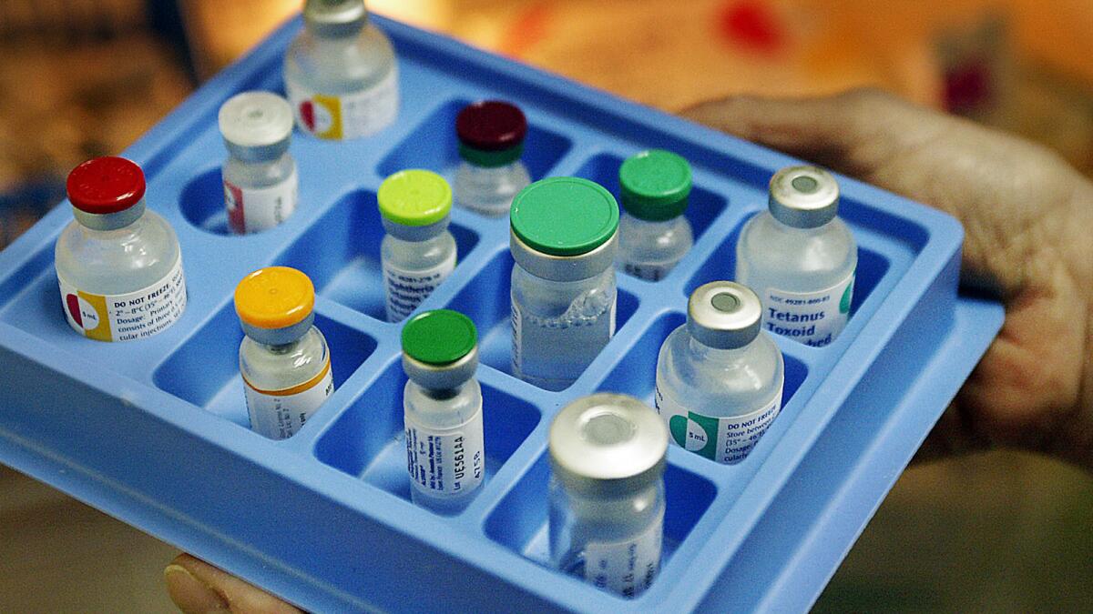 A dozen bottles of childhood vaccines with differently colored tops sit in a blue tray. 