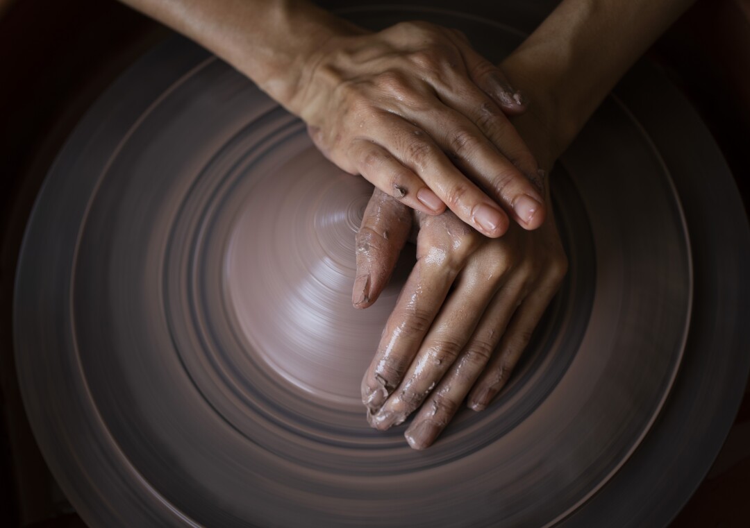 A hand shapes clay on a ceramics wheel