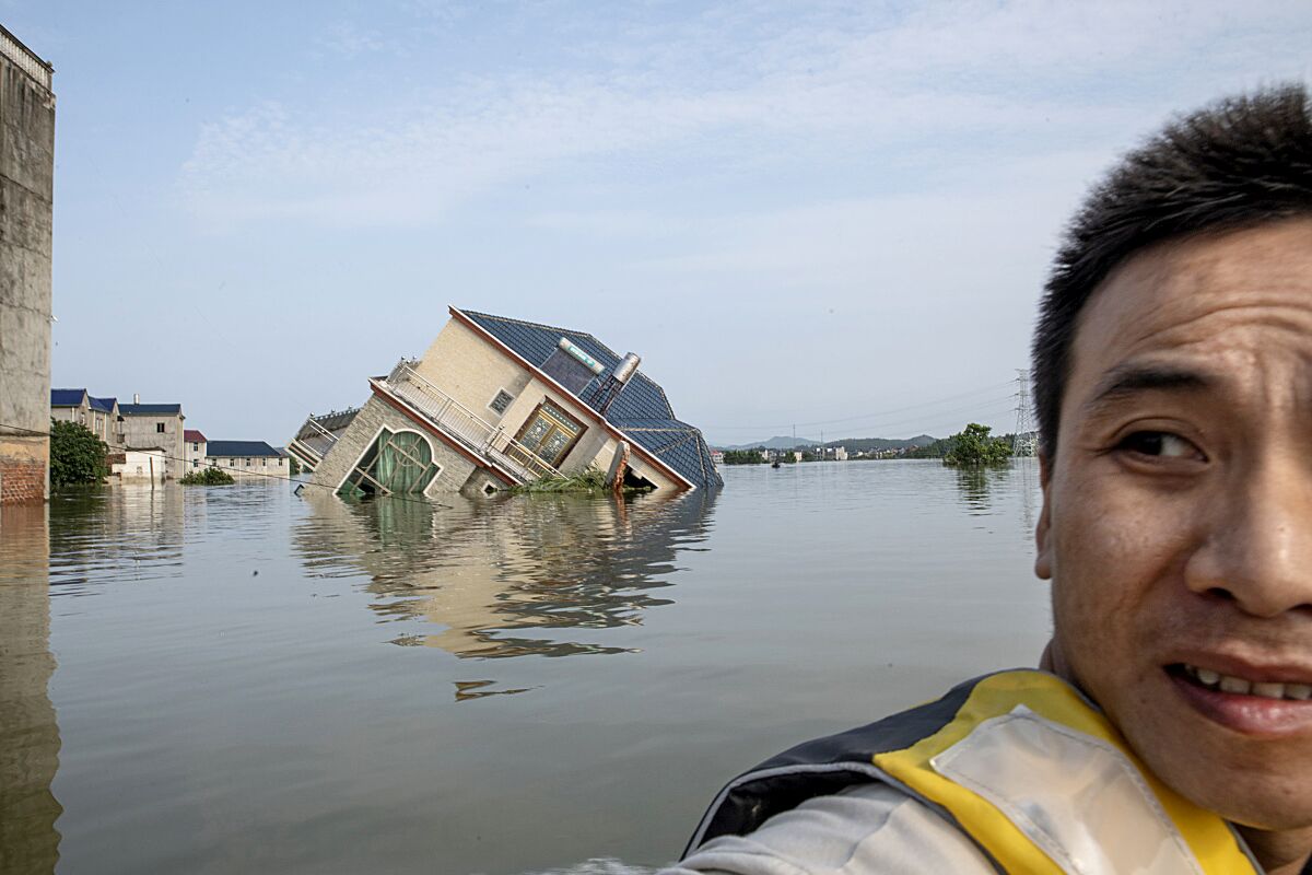Gao, a local villager, sits on a rescue boat in front of a flooded house that fell into a river in China's Jiangxi province.
