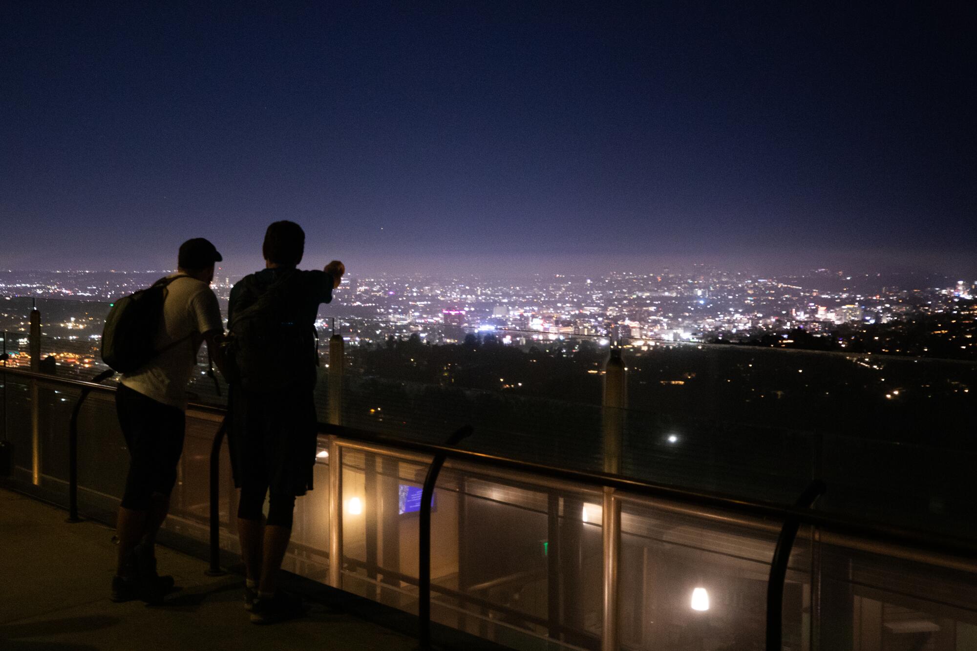 A silhouette of two men overlooking the city of Los Angeles at night, from Griffith Observatory.