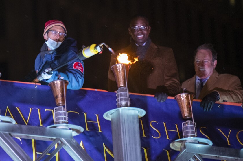 Honorary lamplighter Danny Fenster, an American journalist recently freed from prison in Myanmar, lights the center candle in the giant Menorah sculpture in Campus Martius to kick off Chanukah. With him are Lt. Gov. Garlin Gilchrist II and Detroit Mayro Mike Duggan. The Menorah in the D 11th annual lighting event in Campus Martius Park in downtown Detroit officially begins Chanukah in Michigan on Sunday, Nov. 28, 2021. (John T. Greilick/Detroit News via AP)