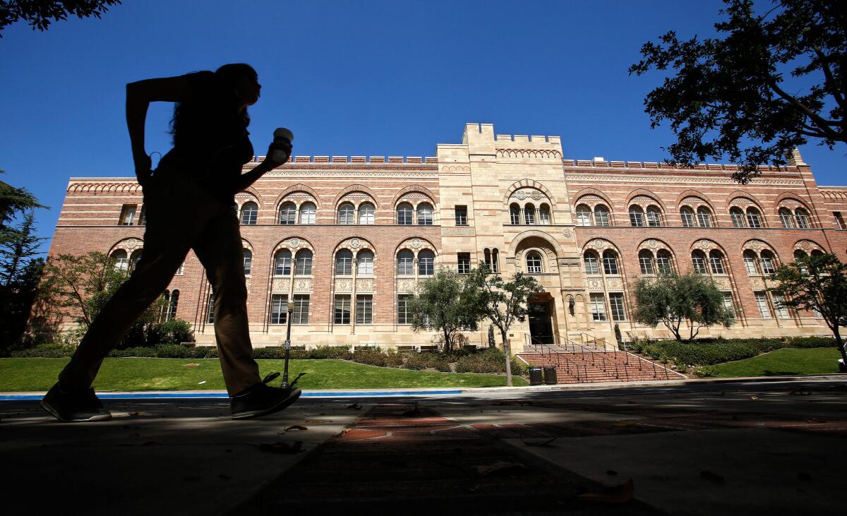 A person seen in profile walks in front of a red brick academic hall at UCLA