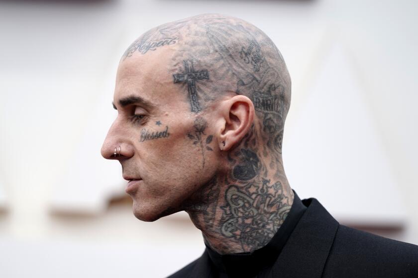 A side view of a bald man whose head, neck and face are covered in tattoos