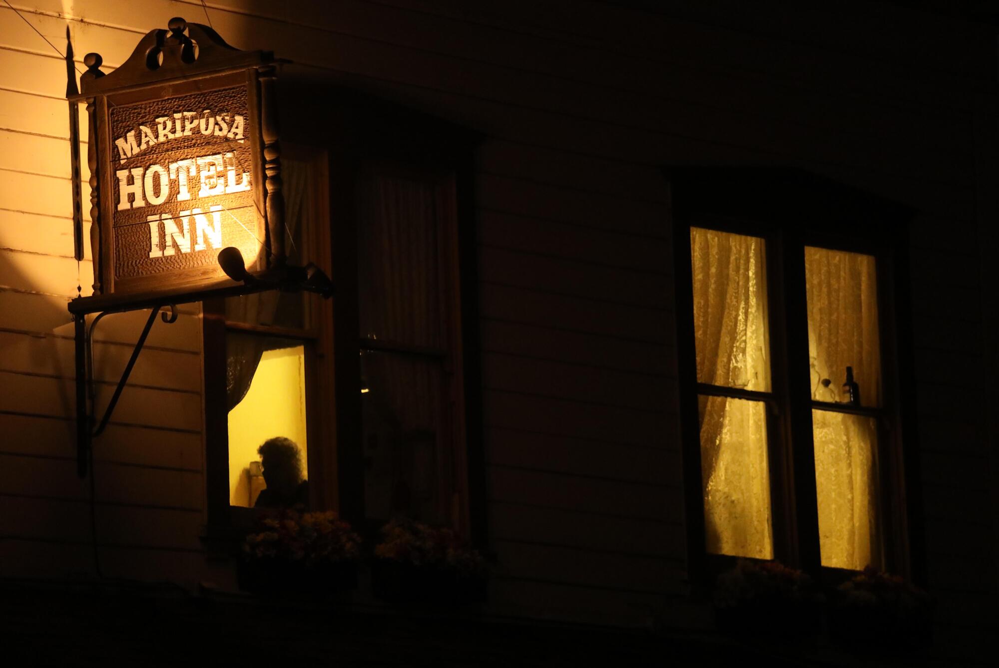 A woman peers out from the second story of the Mariposa Hotel Inn along Highway 140