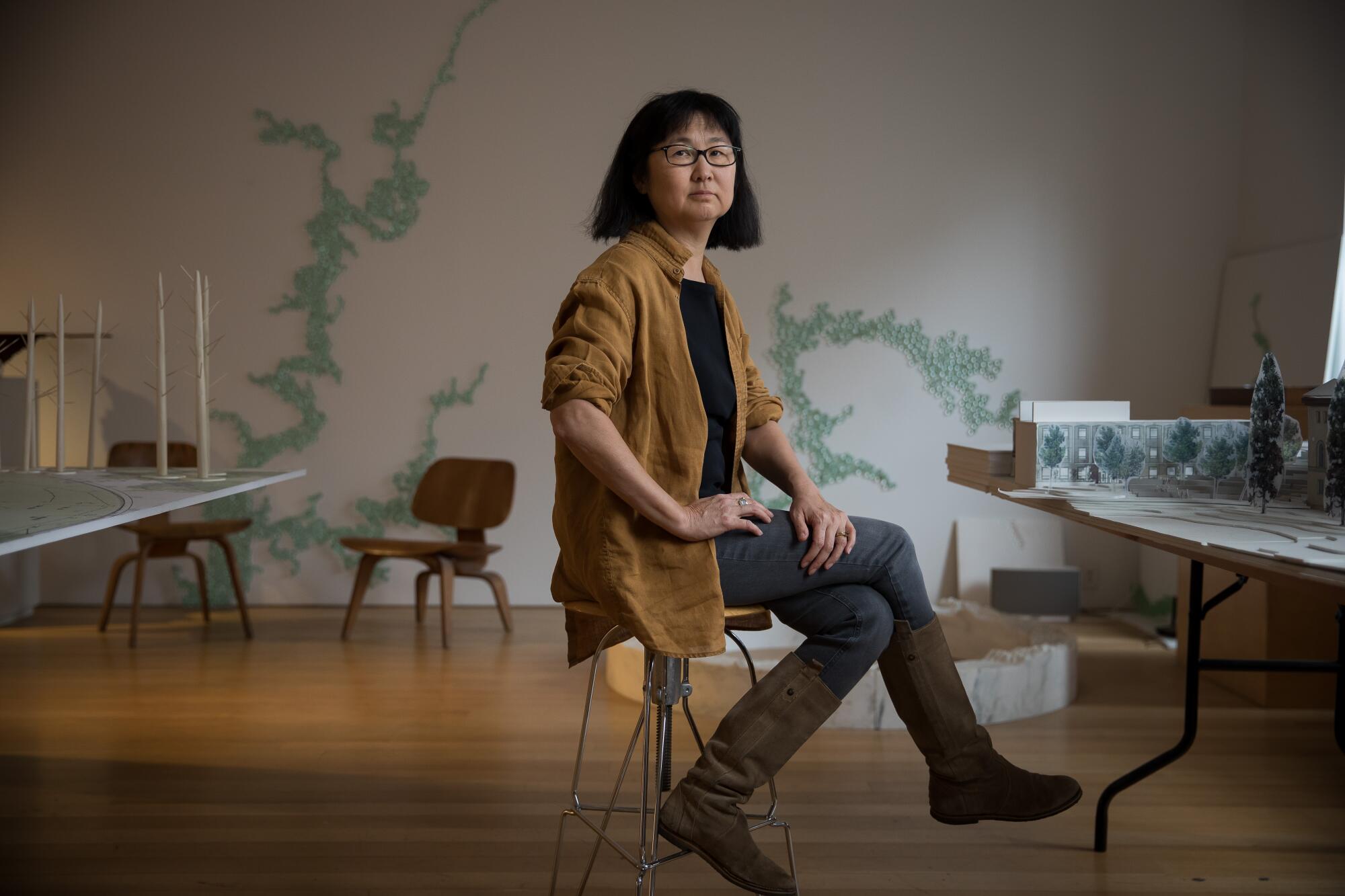 Maya Lin seated in her studio between models of "Ghost Forest" and the Smith College Library