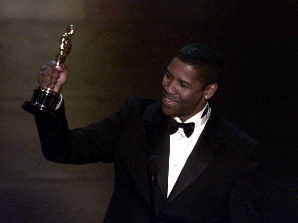 A man in a tux holds up an Oscar 