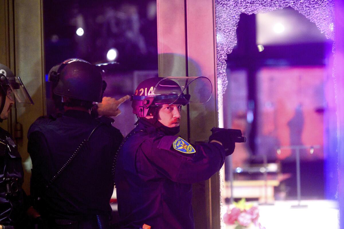 A police officer aims his weapon while clearing a vandalized Victoria's Secret store in San Francisco on Saturday.