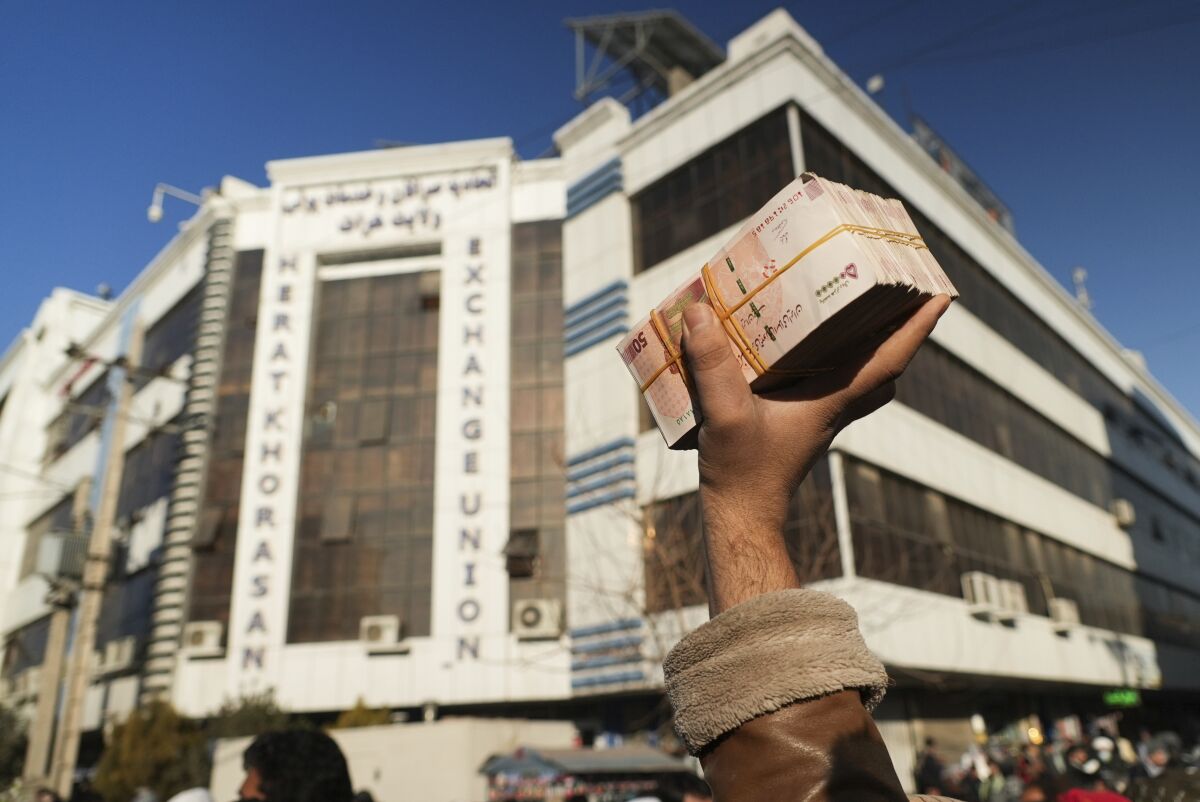 An Afghan money changer holds a stack of Iranian currency at Khorasan market in Herat, Afghanistan, Wednesday, Dec. 15, 2021. The value of Afghanistan's currency is tumbling, exacerbating an already severe economic crisis and deepening poverty in a country where more than half the population already doesn't have enough to eat. (AP Photo/Mstyslav Chernov)