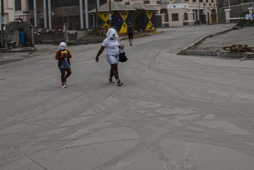 A woman and a girl walk wearing protective head coverings walk on a street covered with volcanic ash a day after the La Soufriere volcano erupted, in Kingstown, on the eastern Caribbean island of St. Vincent, Saturday, April 10, 2021. (AP Photo/Lucanus Ollivierre)
