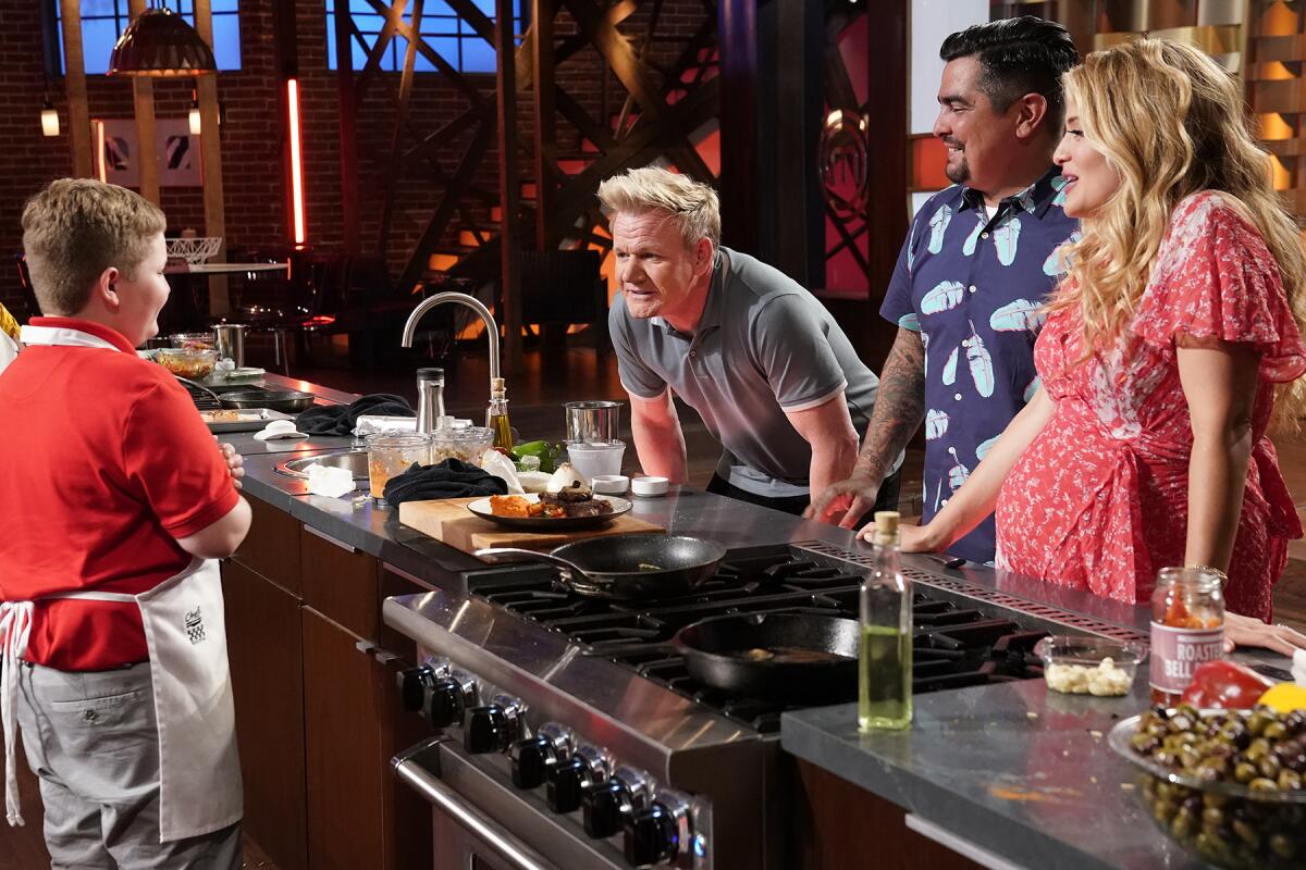 Three adults talk to a teen boy who's standing at an elaborate kitchen setup.