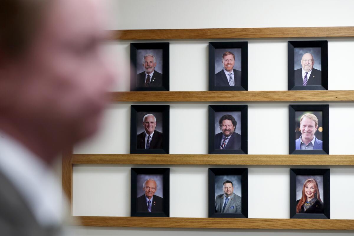 A person, blurry and close to the camera, stands at right in front of nine headshot portraits of people.