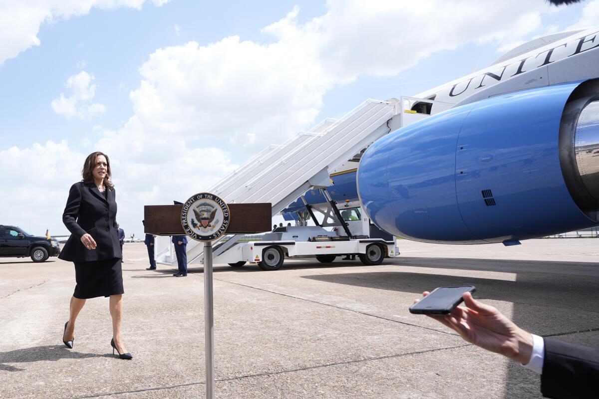 Kamala Harris walks on an airport tarmac near a large jet, approaching a speaker's stand with the vice presidential seal