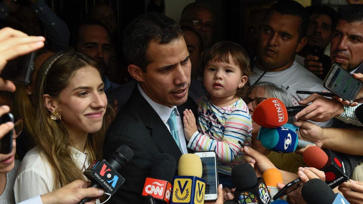 Opposition leader and self-proclaimed interim president Juan Guaido talks to the press as he holds his daughter, Miranda, while standing next to his wife, Fabiana, outside their home Thursday.