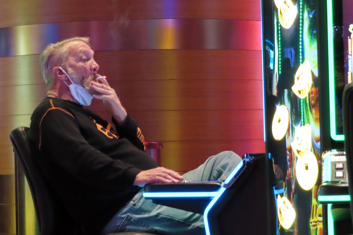 FILE - A man smokes while playing a slot machine at the Ocean Casino Resort in Atlantic City, N.J., on Feb. 10, 2022. A report issued Friday, June 17, 2022, by a Las Vegas gambling research company suggested that ending smoking in casinos will not result in significant financial harm to the businesses.. (AP Photo/Wayne Parry, File)