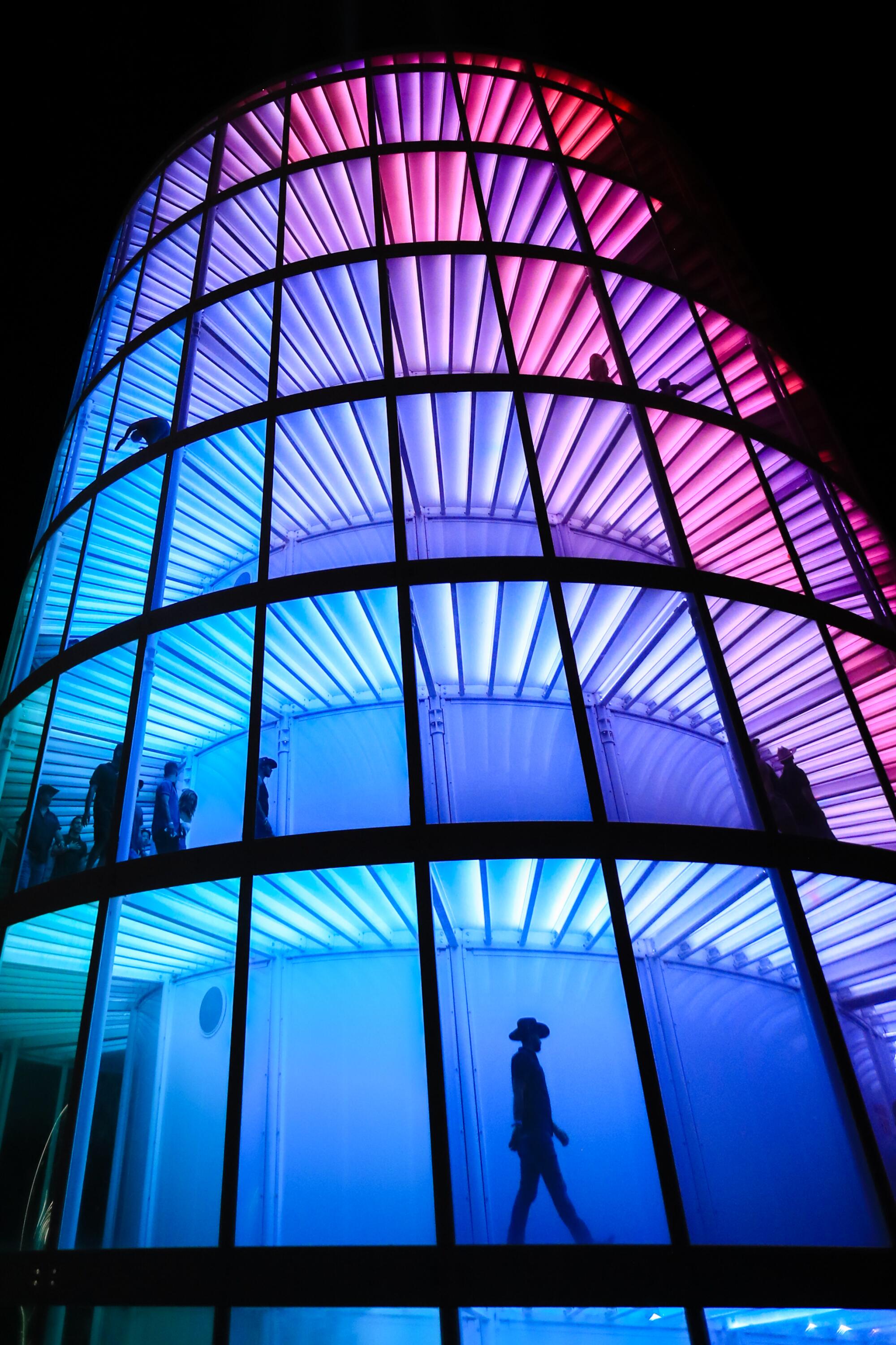 A festival goer is silhouetted while walking at night through a blue, purple and pink lighted tower.